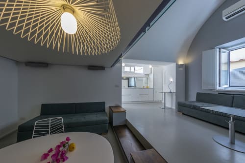 Suite moderna open-plan con sedute nere, cucina bianca, lampada geometrica al soffitto e vista mare