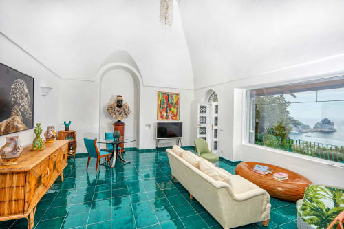 Lussuoso salotto dell'hotel Capri con piastrelle in maiolica color turchese, divano color crema, mobili in legno e vista panoramica sul mare