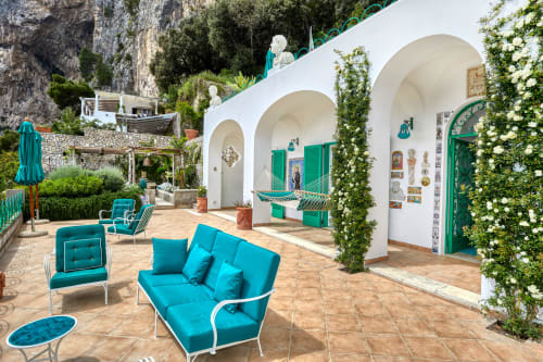 Terrazza La Conciergerie Capri con sedute turchesi, archi bianchi, persiane verdi e muri ricoperti di edera