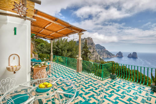 Terrazza di La Conciergerie Capri con piastrelle turchesi, pergolato in legno e i Faraglioni sullo sfondo