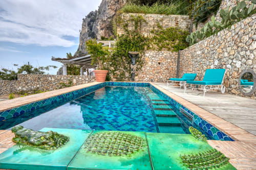 Lussuosa piscina di La Conciergerie Capri con acqua turchese, terrazza in legno, muri in pietra e vista sul mare