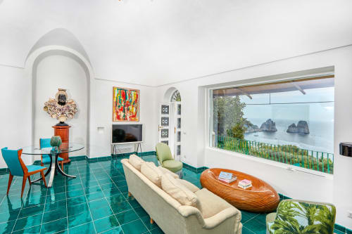 Suite lussuosa a La Conciergerie Capri con vista mare, pavimenti in maiolica turchese, divano crema e paesaggio costiero