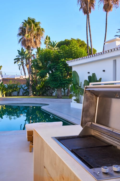 Lussuosa cucina all'aperto in riva alla piscina di La Conciergerie Capri con palme e vista sul giardino mediterraneo