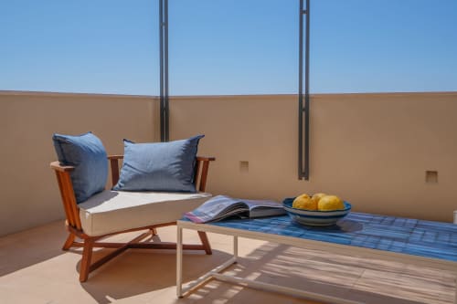 Terrazza soleggiata a La Conciergerie Capri con sedia in legno, cuscini blu, rivista e limoni freschi affacciati sul mare