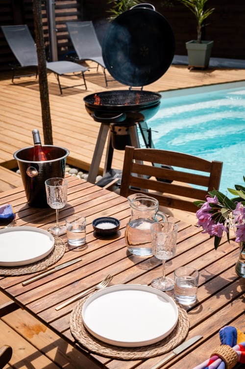 Espace de dining en bord de piscine à la Villa Eden Bleu avec table dressée, barbecue et bassin à Biscarrosse