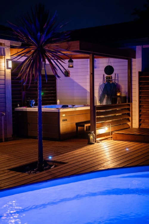Terrasse piscine de la Villa Eden Bleu la nuit, avec bain à remous illuminé, décor bois et palmier à Biscarrosse