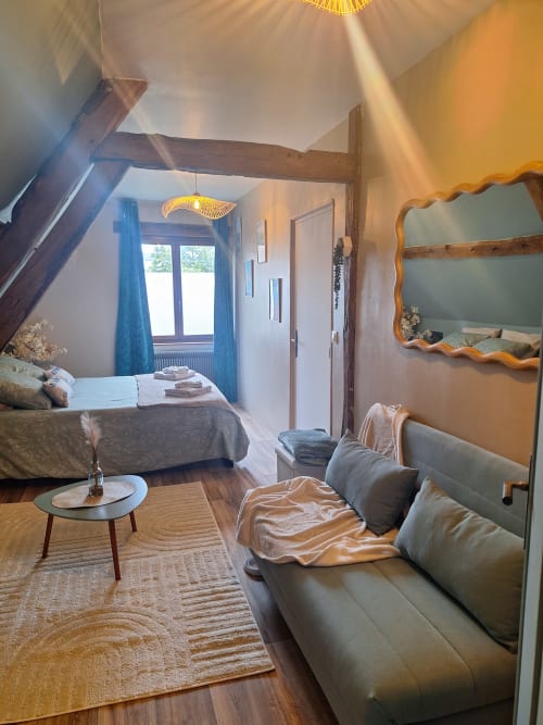 Chambre cosy de la Chambre d'Hortense avec lit, coin salon, miroir, poutres en bois et vue sur le jardin à Sailly-Flibeaucourt