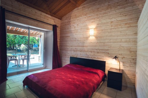 Chambre moderne avec literie rouge et murs en bois à la villa Le Maquis Plage, vue terrasse sur le jardin et le lac