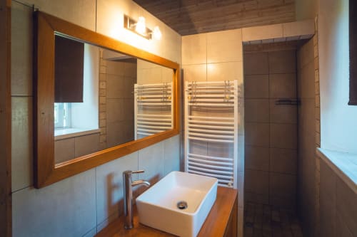 Salle de bain moderne avec plan de travail en bois, miroir encadré, porte-serviettes chauffant et douche italienne à la villa Le Maquis Plage