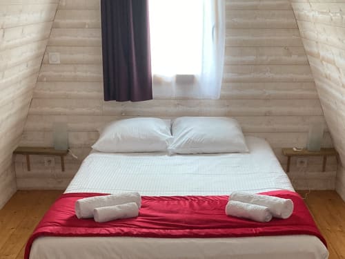Cozy bedroom in Lodge Bois Confort at Domaine des Piéris, Grandcamp-Maisy, with white pillows, red blanket, and garden view