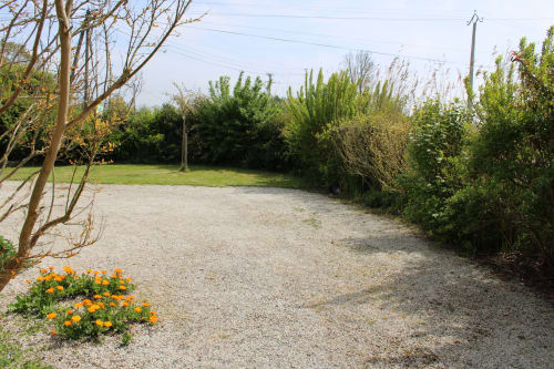 Gravel pathway through lush garden with green lawn, hedges, and yellow flowers at Domaine des Piéris cottage in