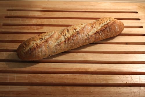 Baguette aux graines fraîchement cuite sur planche à découper en bois au Domaine des Piéris à Grandcamp-Maisy, France