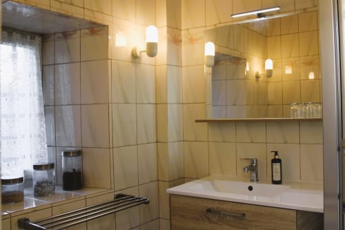 Modern bathroom at Domaine des Piéris with beige tile walls, white sink, mirror, and contemporary lighting fixtures