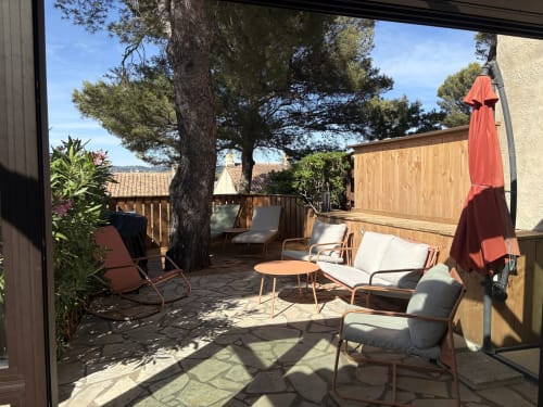Terrasse ensoleillée du Mazet Cavalaire avec chaises longues, terrasse en bois, parasol rouge et arbres matures à Cavalaire-sur-Mer