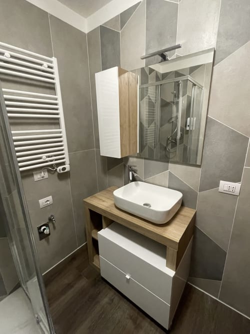 Bagno moderno nell'appartamento Varenna by Foot con vanità in legno, lavabo bianco, piastrelle grigie e scaldarughe riscaldato
