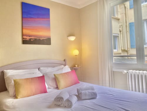 Bright family bedroom at Hôtel Maison Richet with sunset artwork, gradient pillows, and city views through large windows