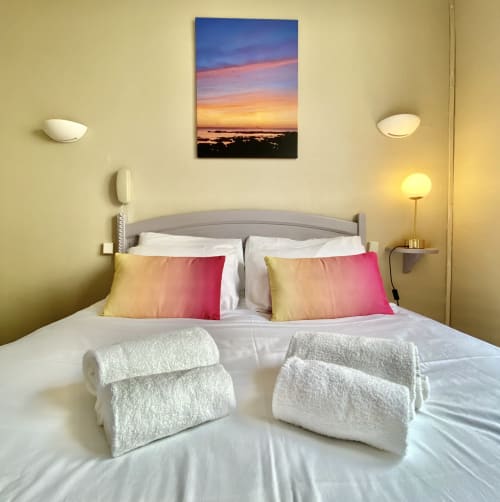 Modern bedroom at Hôtel Maison Richet in Les Sables-d'Olonne with sunset artwork, white bedding, pink pillows, and rolled