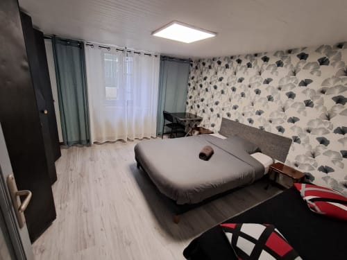 Chambre moderne à l'appartement NancyRoom à Vandœuvre-lès-Nancy avec lit, bureau, vue sur la ville et papier peint à motifs géométriques