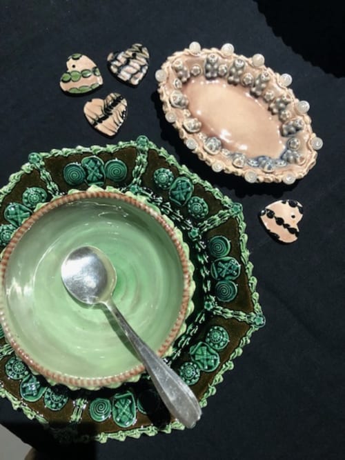 Élégante vaisselle au Domaine de l'Ocrerie : bol en céramique verte avec cuillère et assiette décorée de perles sur fond sombre.