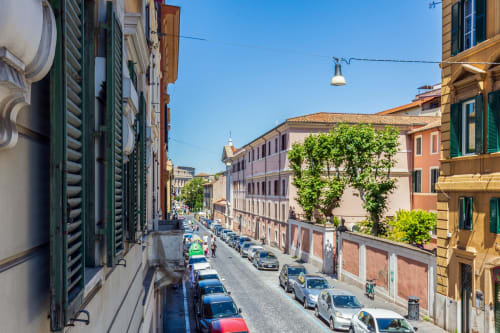 Vista soleggiata di una strada romana da Petra Apartments con auto parcheggiate, edifici storici e facciata ricoperta di edera