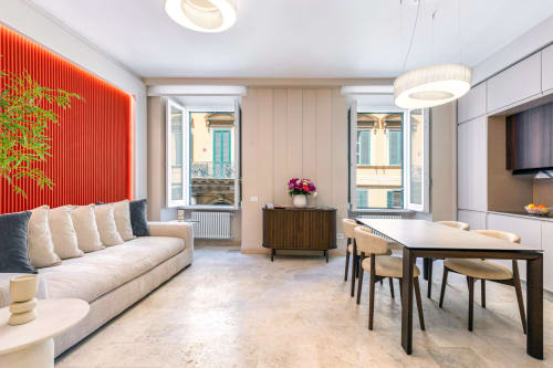 Zona living moderna presso Petra Apartments Roma con divano beige, parete accent rossa, tavolo da pranzo e vista sulla città