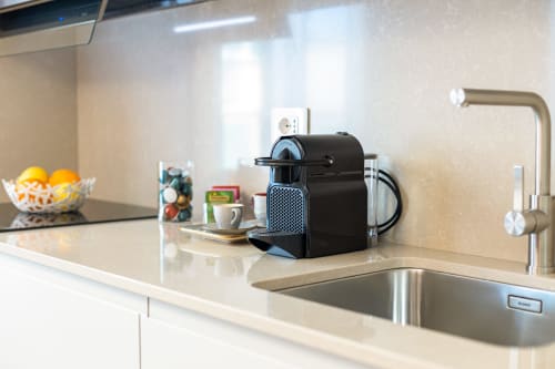 Moderno bancone cucina alle Petra Apartments Roma con macchina espresso, lavello e vista città dalle finestre luminose