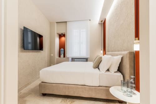 Camera moderna Petra Apartments Roma con letto, TV a parete, pareti beige e illuminazione rossa d'accento