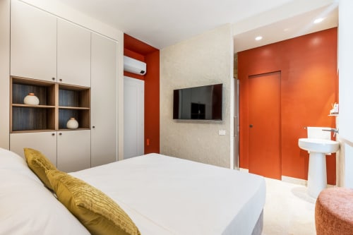 Camera moderna di Petra Apartments Roma con parete accent arancione, TV, letto bianco e bagno ensuite