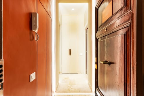 Corridoio Petra Apartments Roma con pareti arancioni, porta in legno e ingresso luminoso che conduce a moderno armadio bianco