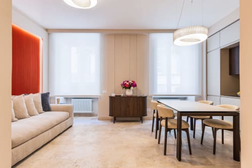 Soggiorno e zona pranzo moderni negli Appartamenti Petra a Roma con divano beige, tavolo in legno, lampade a sospensione e vista sulla città