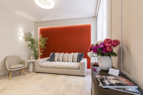 Soggiorno moderno degli Appartamenti Petra Roma con divano beige, parete accent rossa, peonie rosa e vista sulla città