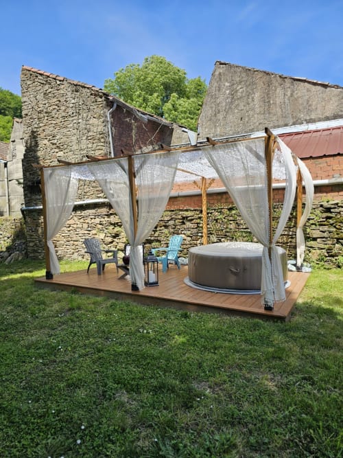Bain à remous extérieur avec dais à rideau blanc sur terrasse en bois à la Bastide du Thoré