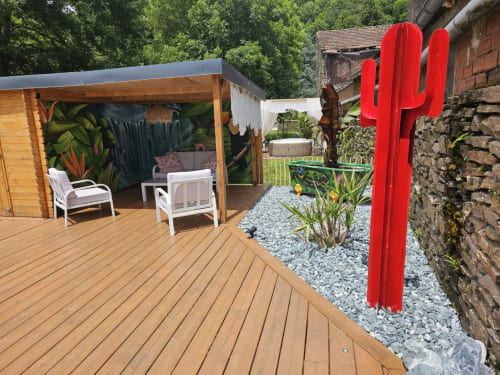 Terrasse en bois avec chaises longues à la Bastide du Thoré, sculpture de cactus rouge, bâtiments en pierre à Labastide-Rouairoux
