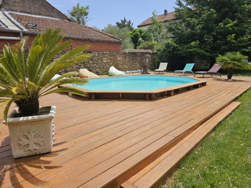 Piscine et terrasse en bois de la Bastide du Thoré avec transats, palmiers et bâtisses en pierre à Labastide-Rouairoux