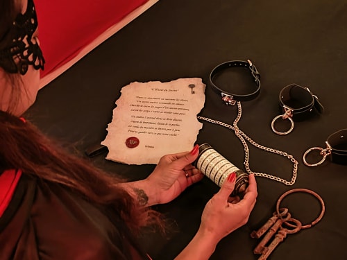 Hand holding wine bottle with BDSM accessories and romantic letter at Les Secrets de Winna love cottage in Nouvelle-Aquitaine