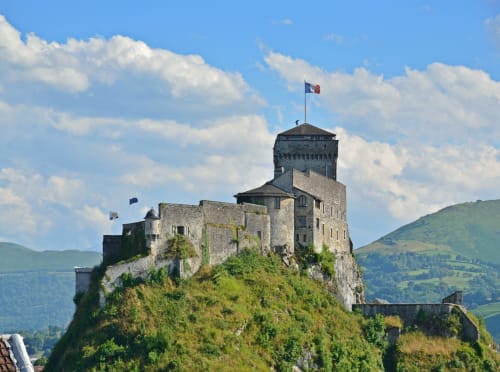 Historisches Schloss auf Hügel über Lourdes mit Steinbefestigungen und französischer Flagge