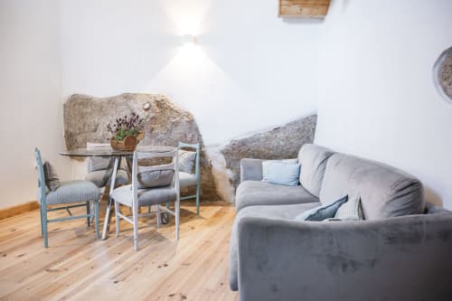 Quarto rural da Casa das Jardas com sofá cinzento, paredes de pedra, piso de madeira e área de refeições em Ladoeiro