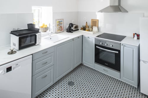 Cozinha moderna com armários cinzentos, balcões brancos e ladrilhos preto e branco em Casa das Jardas, hospedagem rural