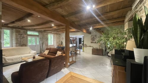 Spacieux séjour ouvert dans un gîte de Corrèze avec poutres en bois, mobilier marron, plantes et murs en pierre