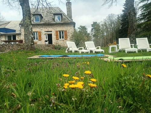 Chaumière en pierre dans les bois de Corrèze avec chaises longues blanches, jardin fleuri de fleurs jaunes et pelouse verdoyante
