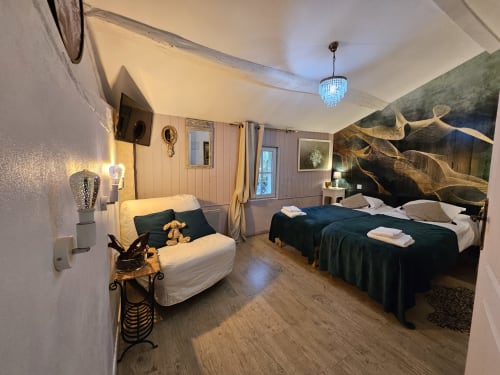 Geräumiges Schlafzimmer im Manoir Lacustre mit zwei Betten, Sitzbereich und künstlerischer Wanddekoration in Queyrac