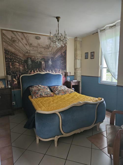 Elegantes Schlafzimmer im Manoir Lacustre mit blauem Polsterbett, gelber Steppdecke, Kristalllüster und Gartenblick