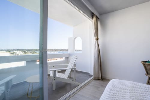 Dormitorio estudio moderno con balcón vista al mar en Formentera Especial, La Savina. Silla Adirondack blanca frente a la costa