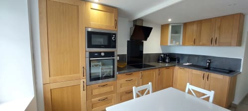 Cuisine moderne avec meubles en bois, plan de travail noir, électroménagers en acier inoxydable et table à manger dans l'appartement Gîte Bambou