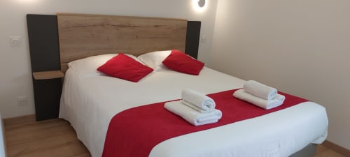 Chambre moderne au Mas de Trépeloup à Alès avec literie blanche, oreillers rouges, serviettes et tête de lit en bois