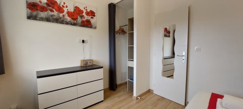Chambre élégante du Gîte Coquelicot à Alès avec mobilier blanc, œuvre de coquelicot rouge, armoire miroir et bois