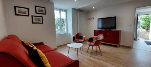 Salon moderne du Gîte Coquelicot avec canapé rouge, télévision écran plat, chaises de salle à manger et vue sur le jardin, à Alès