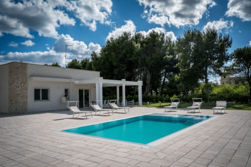 Modern villa in Ferrara with turquoise pool, white loungers, and pergola terrace surrounded by trees