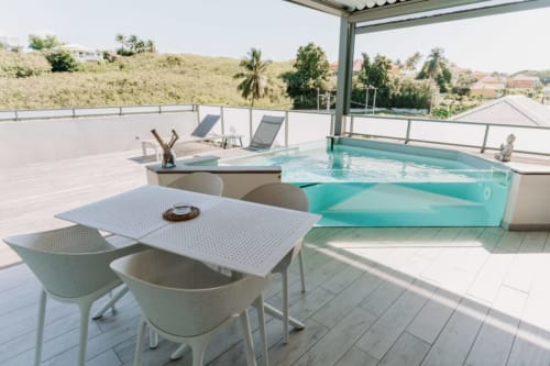 Terrasse de luxe sur le toit d'Habitation l'SEO à Sainte-Anne avec piscine turquoise, table de repas, transats et vue tropicale