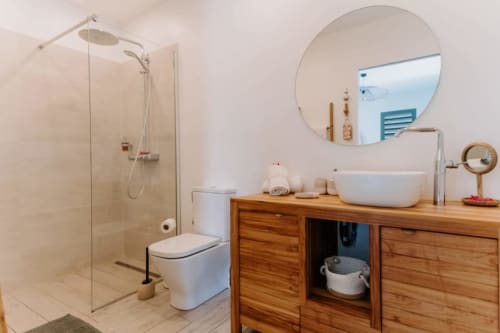 Salle de bain moderne à Habitation I'SEO avec douche vitrée, meuble-lavabo en bois, vasque blanche et miroir rond